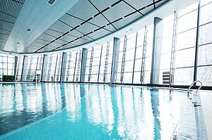 Innenaufnahme eines modernen Hallenbades mit großen Glasflächen; das Schwimmbecken ist menschenleer.