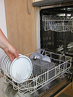 Eine Hand nimmt einen Teller aus einer geöffneten Geschirrspülmaschine.