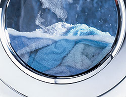 Sichtfenster einer Waschmaschine, halb gefüllt mit Handtüchern und schaumigem Wasser