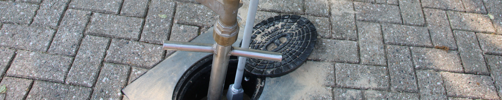 Geöffneter Hydranten-Deckel im Verbundsteinpflaster mit eingesetztem Standrohr.